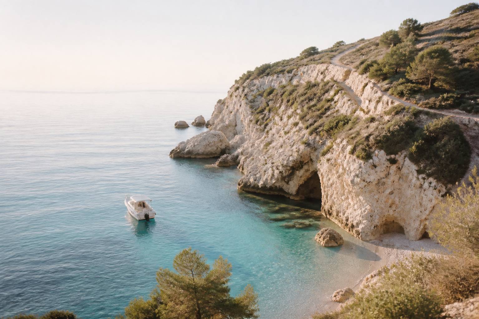 Petit bateau blanc approchant une crique rocheuse aux eaux claires, falaises de calcaire et pins