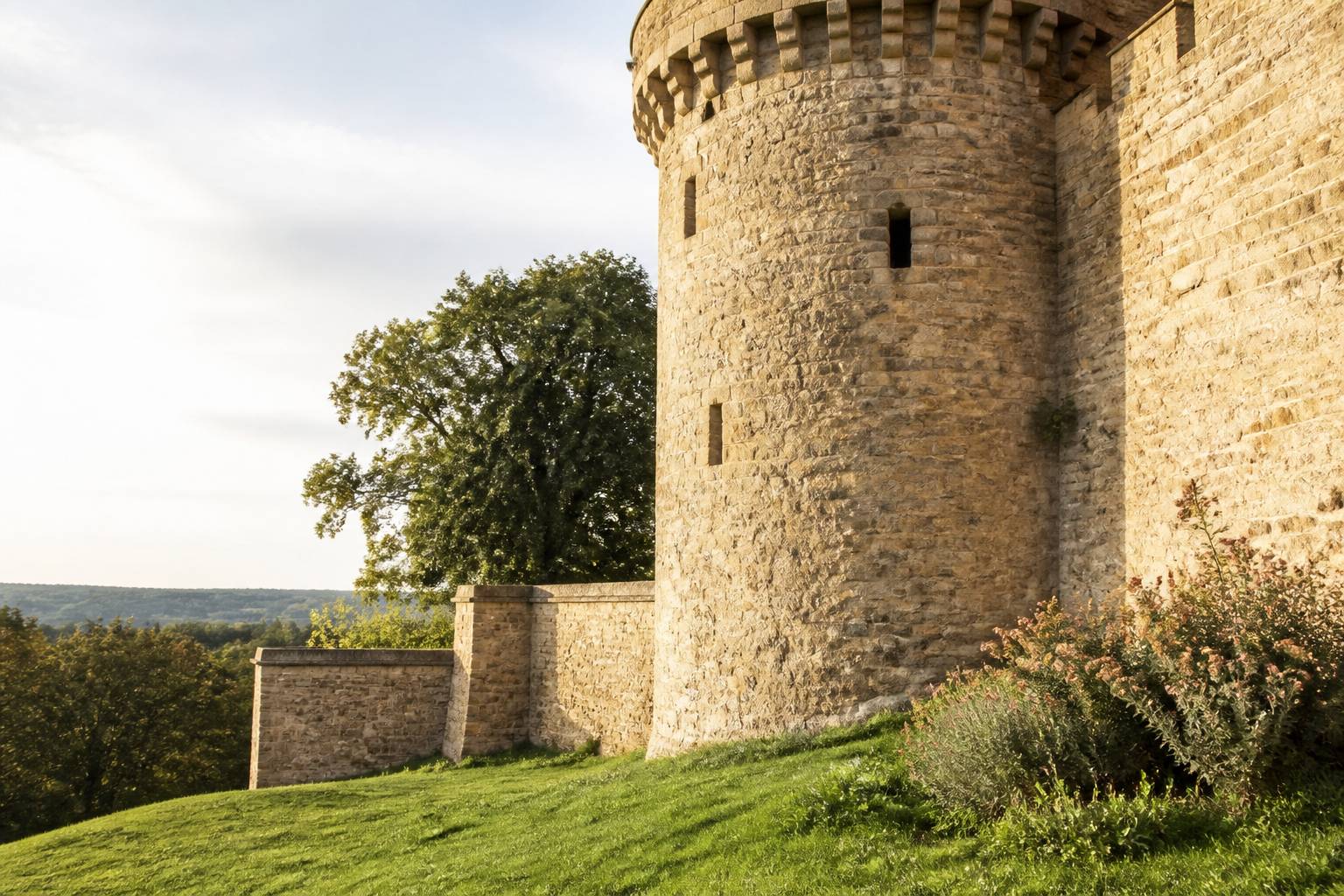 Remparts en pierre dorée avec tour ronde et meurtrières d'un château fort
