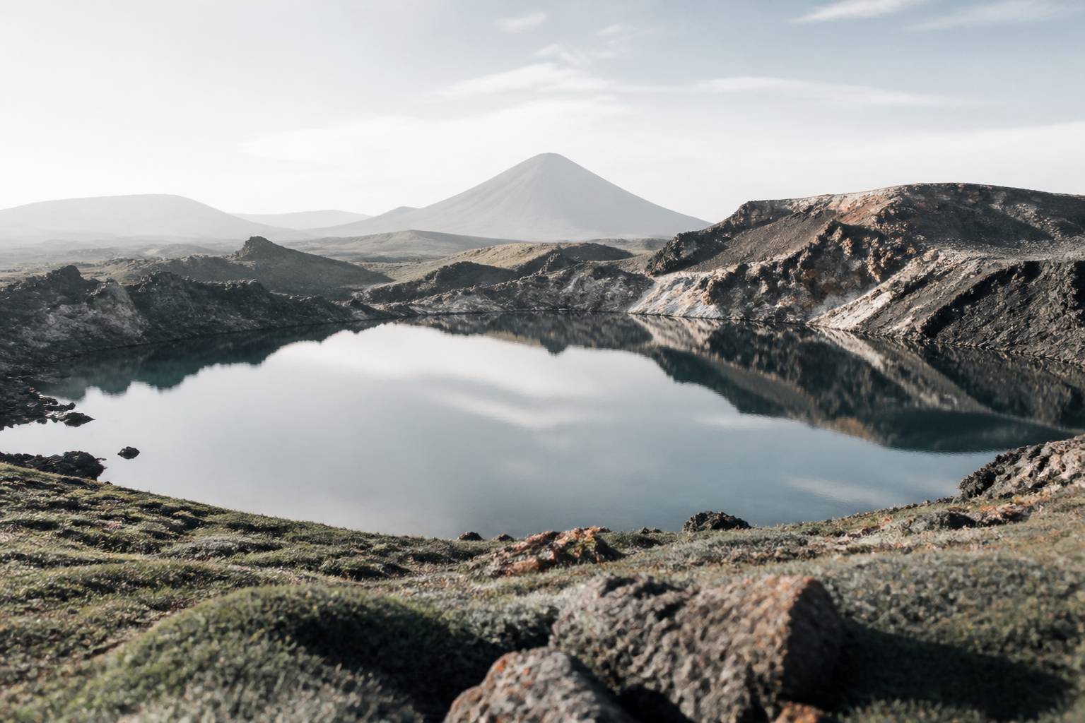 Lac de cratère avec reflets et roches volcaniques sombres au premier plan